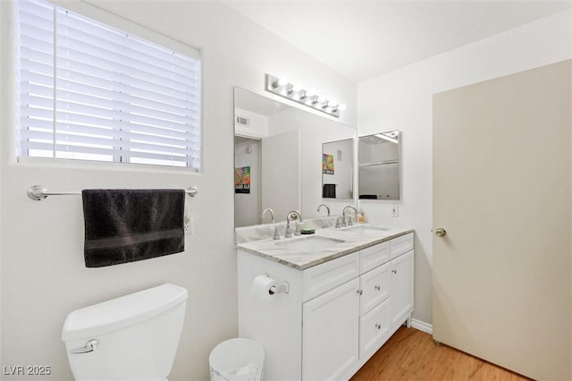 bathroom with double vanity, toilet, wood finished floors, and a sink