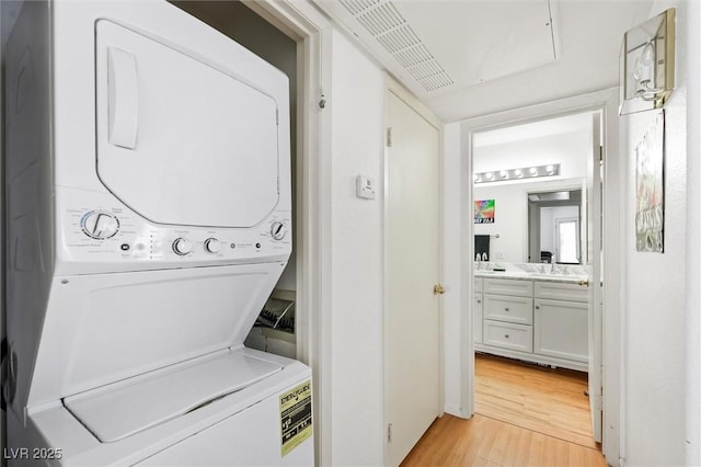 clothes washing area featuring laundry area, light wood-style flooring, and stacked washer and clothes dryer