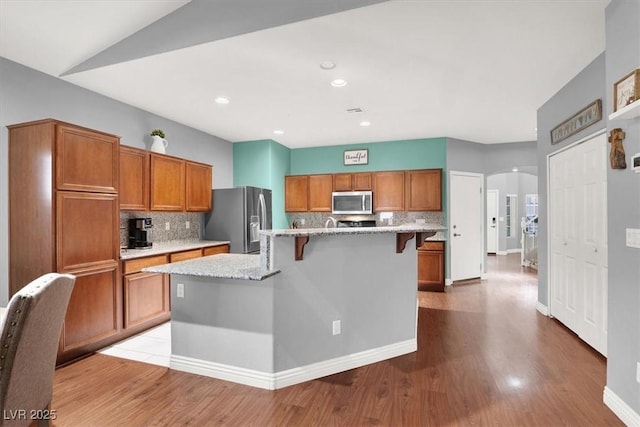 kitchen with a breakfast bar area, brown cabinetry, arched walkways, stainless steel appliances, and light wood-type flooring