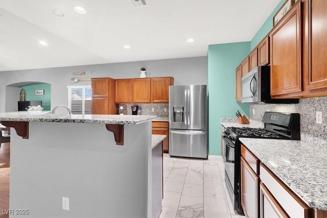 kitchen with a breakfast bar, brown cabinets, marble finish floor, and stainless steel appliances