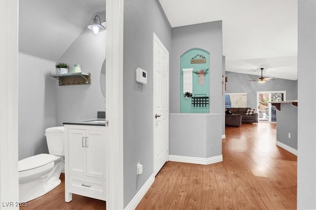 hall featuring baseboards, lofted ceiling, and light wood-style floors