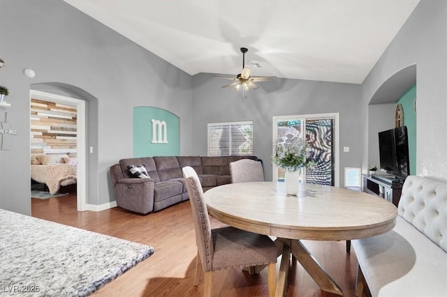 dining space featuring light wood-type flooring, a ceiling fan, arched walkways, baseboards, and vaulted ceiling