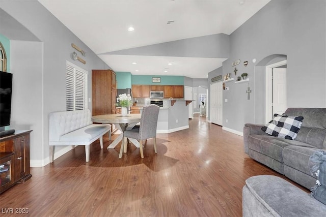 dining area featuring baseboards, recessed lighting, wood finished floors, arched walkways, and high vaulted ceiling