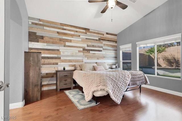 bedroom with wood finished floors, visible vents, baseboards, ceiling fan, and wood walls