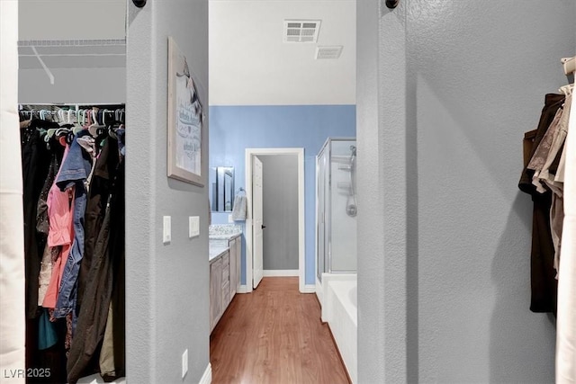 bathroom with visible vents, a stall shower, wood finished floors, baseboards, and a spacious closet