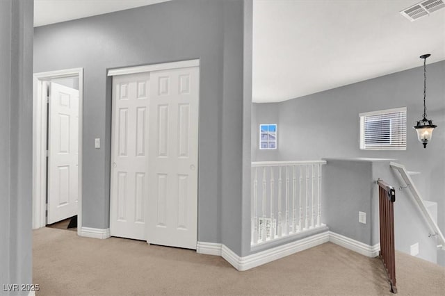 hall with an upstairs landing, visible vents, baseboards, and carpet