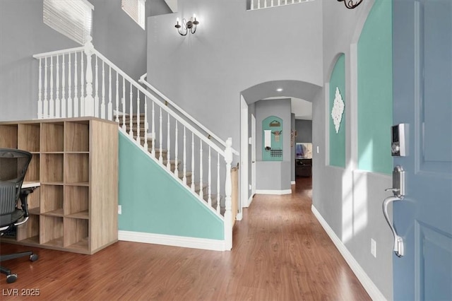 foyer entrance featuring wood finished floors, baseboards, a high ceiling, arched walkways, and stairs