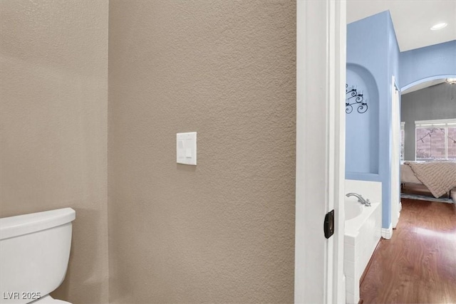 bathroom with toilet, ensuite bathroom, wood finished floors, a bathtub, and a textured wall