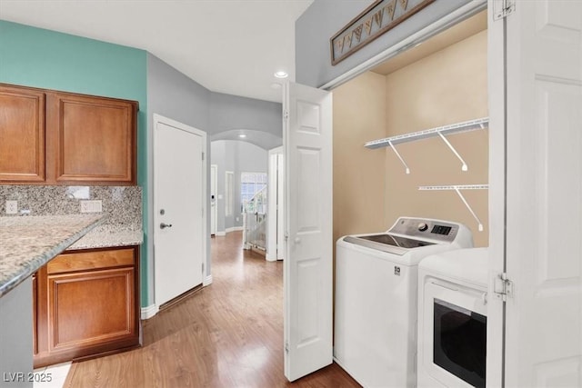 clothes washing area with baseboards, laundry area, light wood-style floors, arched walkways, and washer and dryer