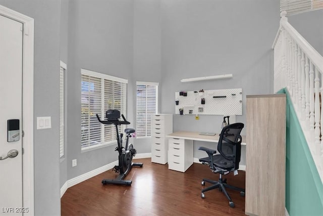 home office featuring baseboards, a high ceiling, and wood finished floors