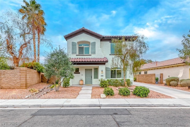 mediterranean / spanish house featuring a tile roof, concrete driveway, fence, and stucco siding