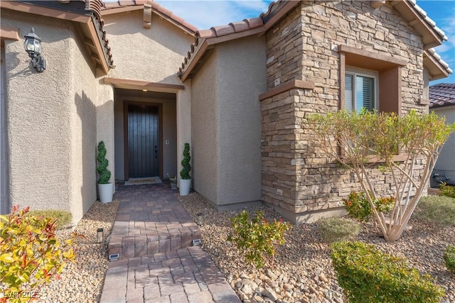 doorway to property featuring stone siding, stucco siding, and a tile roof