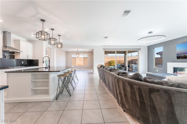 kitchen featuring dark countertops, visible vents, wall chimney range hood, cooktop, and open floor plan