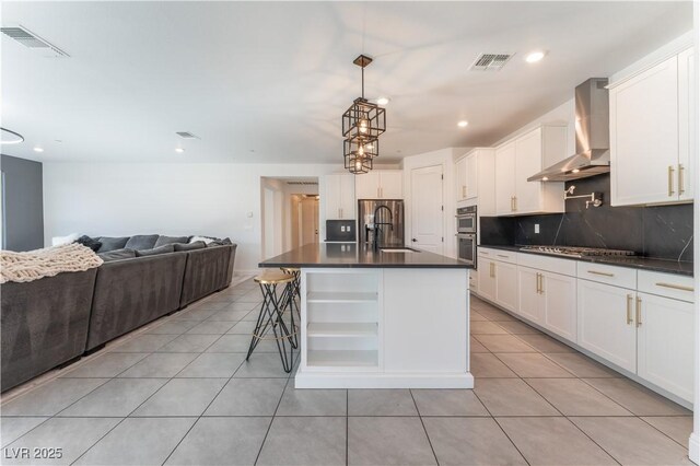 kitchen featuring light tile patterned floors, stainless steel appliances, a sink, dark countertops, and wall chimney range hood