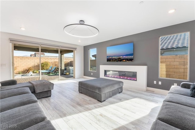 living area featuring recessed lighting, baseboards, wood finished floors, and a glass covered fireplace