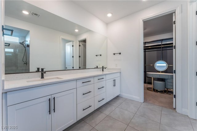 full bath featuring double vanity, tiled shower, visible vents, and a sink