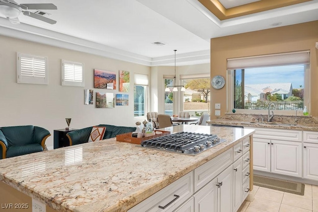 kitchen with a sink, light stone counters, stainless steel gas stovetop, and white cabinets