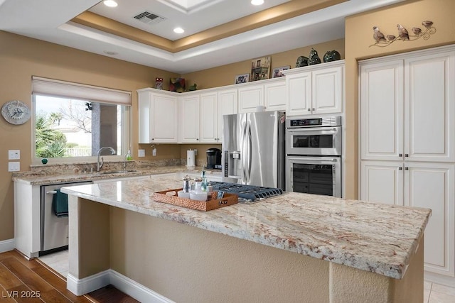 kitchen with visible vents, a sink, a tray ceiling, white cabinetry, and stainless steel appliances