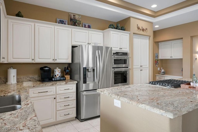 kitchen with a center island, white cabinetry, appliances with stainless steel finishes, light tile patterned flooring, and light stone countertops