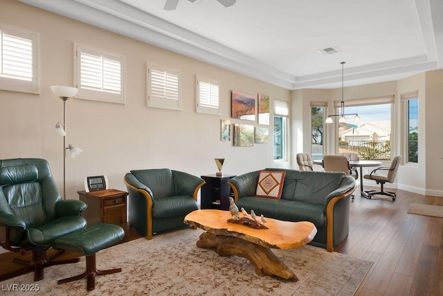 living area featuring visible vents, baseboards, a raised ceiling, and wood finished floors