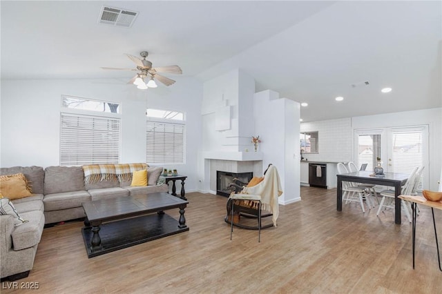 living area featuring visible vents, light wood-type flooring, lofted ceiling, recessed lighting, and a fireplace