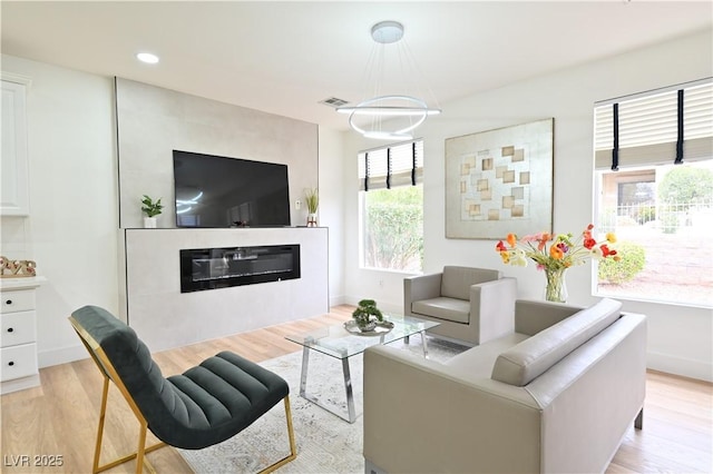 living area featuring recessed lighting, light wood-type flooring, visible vents, and a glass covered fireplace