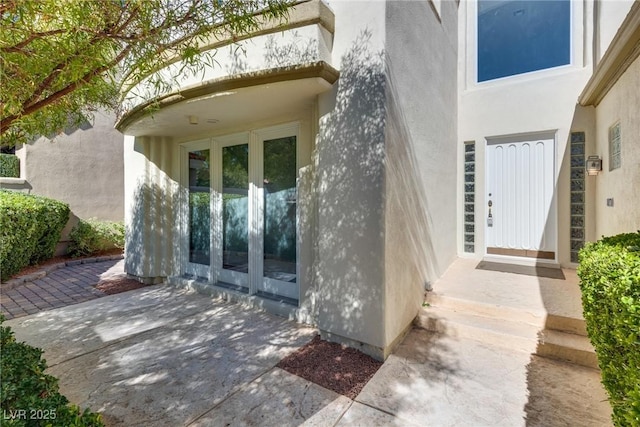 view of exterior entry featuring stucco siding, a patio, and french doors