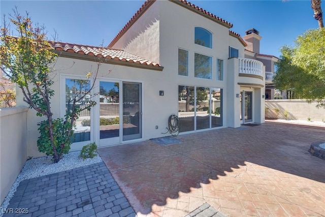 rear view of property featuring a patio, fence, a chimney, stucco siding, and a tiled roof