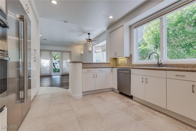 kitchen with stone countertops, a sink, white cabinets, stainless steel dishwasher, and backsplash