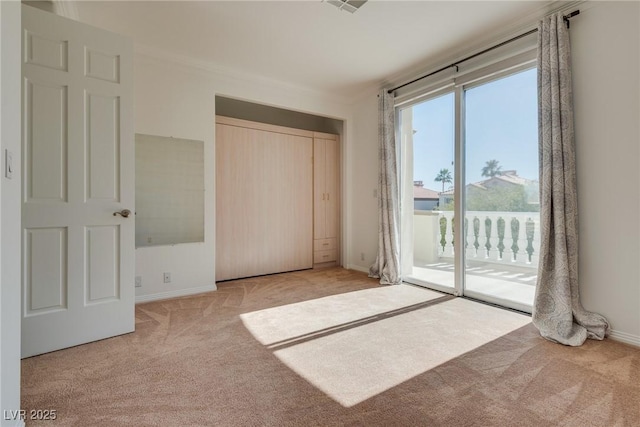 unfurnished bedroom featuring access to outside, a closet, carpet floors, crown molding, and baseboards