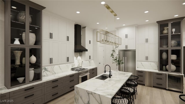 kitchen with wall chimney range hood, a sink, wine cooler, high end appliances, and backsplash