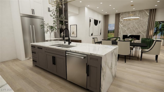 kitchen with light wood finished floors, light stone countertops, a sink, a center island with sink, and appliances with stainless steel finishes