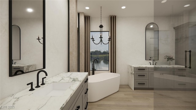 bathroom featuring recessed lighting, wood finished floors, two vanities, a freestanding bath, and a sink