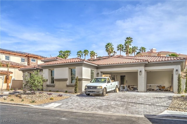 mediterranean / spanish-style house with a garage, a tile roof, stucco siding, and decorative driveway
