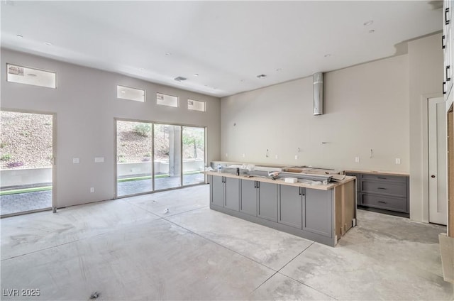 kitchen with light countertops, gray cabinets, a kitchen island, and concrete flooring