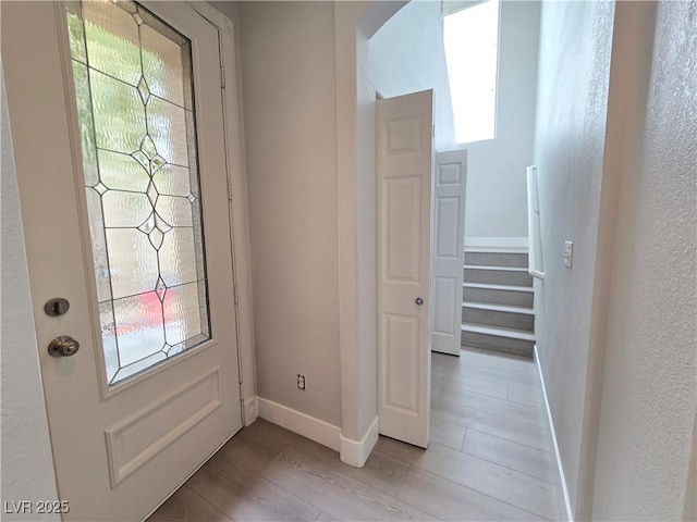 foyer featuring baseboards, arched walkways, and light wood finished floors