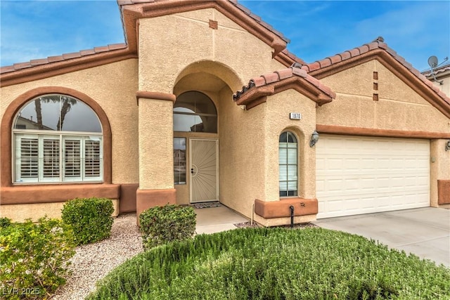 mediterranean / spanish house with concrete driveway, an attached garage, a tile roof, and stucco siding