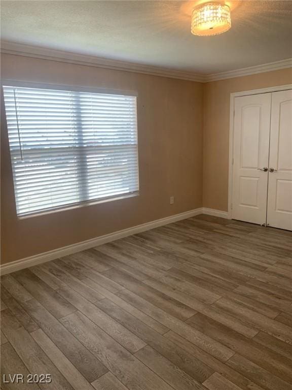 empty room featuring crown molding, wood finished floors, and baseboards