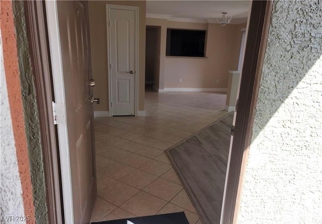 hallway with light tile patterned floors, baseboards, a notable chandelier, and ornamental molding