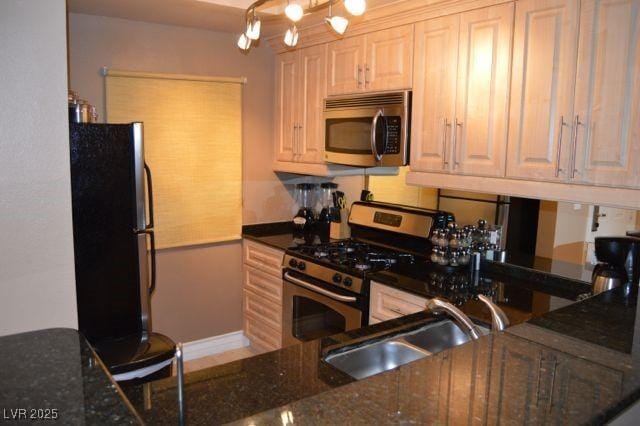 kitchen featuring a sink, appliances with stainless steel finishes, dark stone countertops, and an inviting chandelier