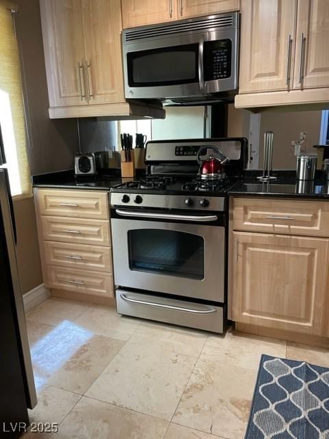 kitchen featuring dark countertops, light brown cabinetry, and stainless steel appliances