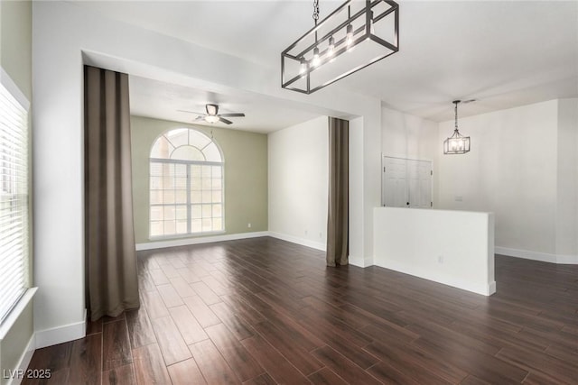 interior space featuring ceiling fan with notable chandelier, dark wood-style floors, and baseboards