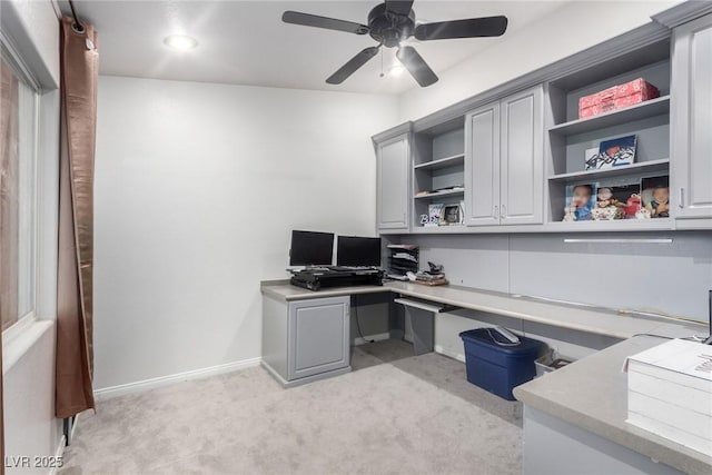 office area featuring baseboards, light colored carpet, ceiling fan, and built in study area