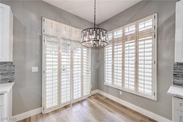 unfurnished dining area featuring light wood finished floors, baseboards, a wealth of natural light, and a chandelier