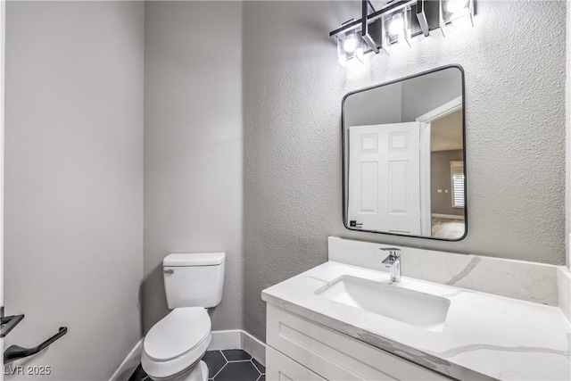 bathroom with tile patterned floors, toilet, baseboards, vanity, and a textured wall