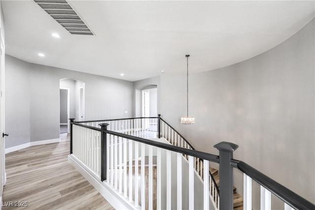 hallway featuring visible vents, an upstairs landing, an inviting chandelier, wood finished floors, and arched walkways