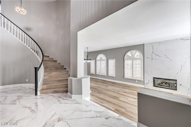 foyer featuring stairway, a notable chandelier, marble finish floor, and a high end fireplace