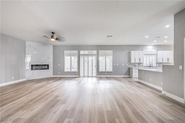 unfurnished living room with ceiling fan, light wood-style floors, visible vents, and a premium fireplace