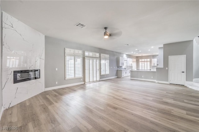 unfurnished living room featuring a ceiling fan, baseboards, visible vents, a premium fireplace, and light wood-type flooring