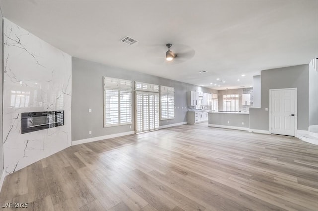 8864 La Manga Ave, Las Vegas, NV 89147 - unfurnished living room featuring a high end fireplace, ceiling fan, light wood-style flooring, baseboards, and visible vents
